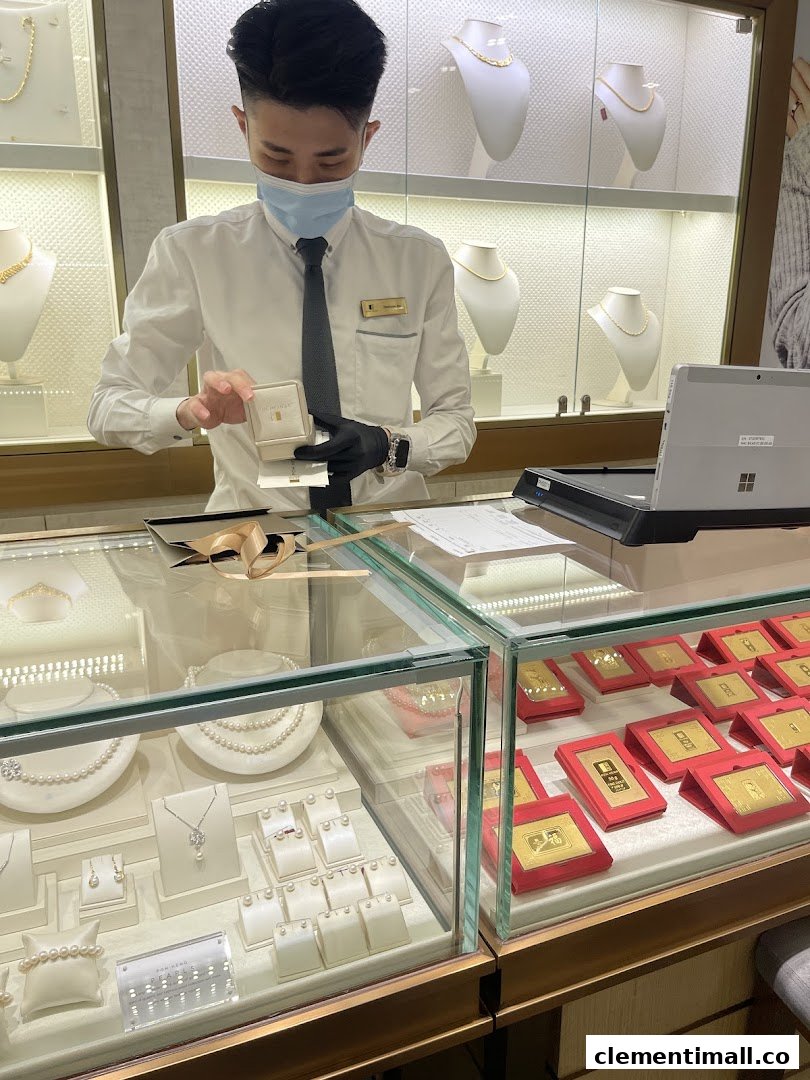 A masked staff member at Poh Heng Jewellery presents a gold item in a display-filled store.