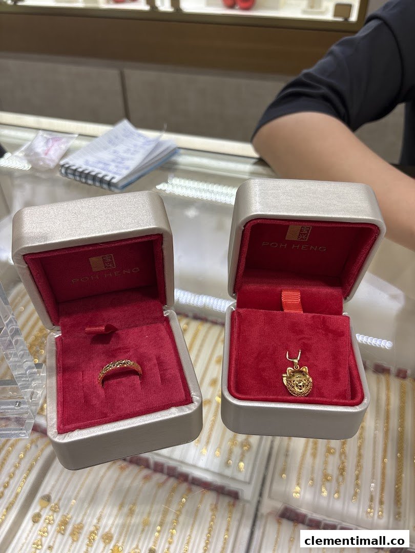 Two open Poh Heng jewellery boxes displaying a gold ring and a gold pendant on a counter.
