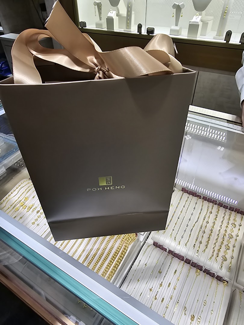 A Poh Heng Jewellery shopping bag on a display counter filled with gold and silver jewellery.