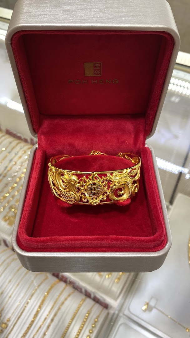 A stunning gold bracelet with intricate dragon and phoenix design displayed in a red Poh Heng Jewellery box.
