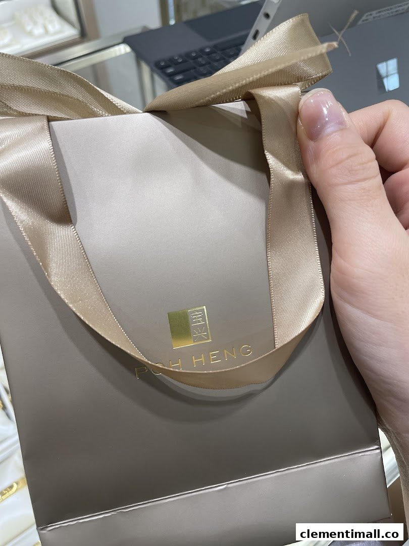 A hand holds a luxurious Poh Heng Jewellery shopping bag with a gold ribbon.