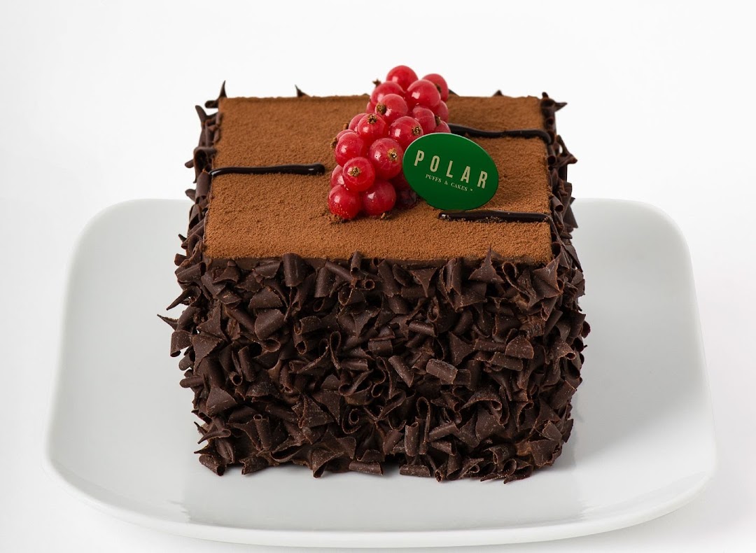 A decadent chocolate cake adorned with red currants and a 'Polar Puffs & Cakes' logo.