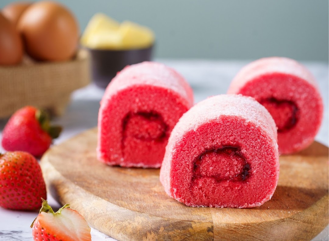 Three vibrant red cake rolls with strawberry filling, alongside fresh strawberries and baking ingredients.