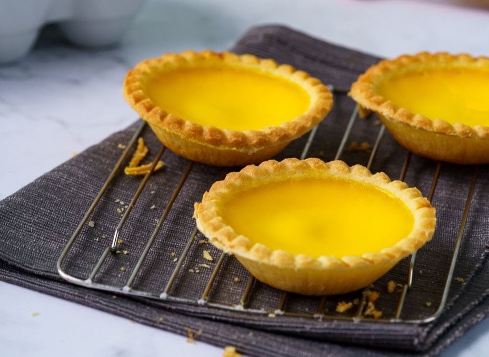 Three golden egg tarts with flaky crusts cooling on a wire rack.