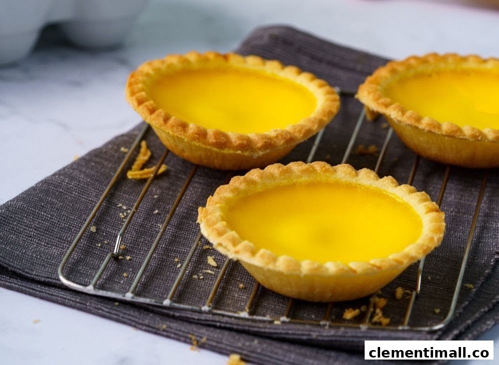 Three golden egg tarts with flaky crusts cooling on a wire rack.