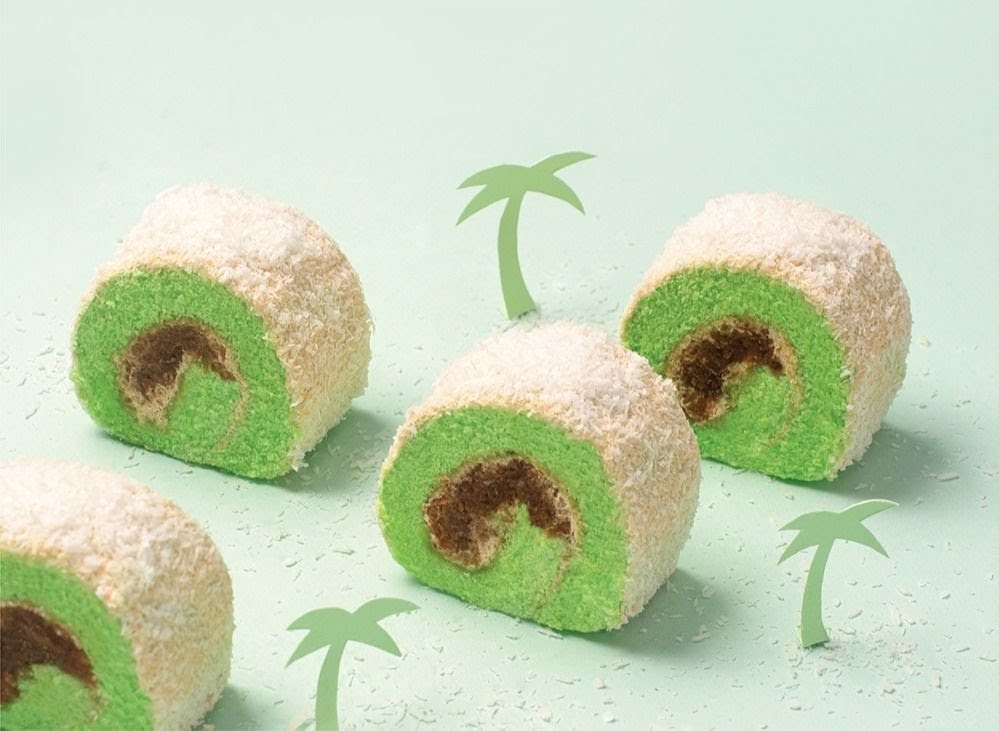 Several vibrant green pandan swiss rolls, coated in coconut flakes, on a light green background.