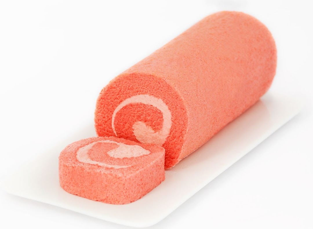 A vibrant pink cake roll with a slice cut, showcasing its creamy swirl filling on a white plate.