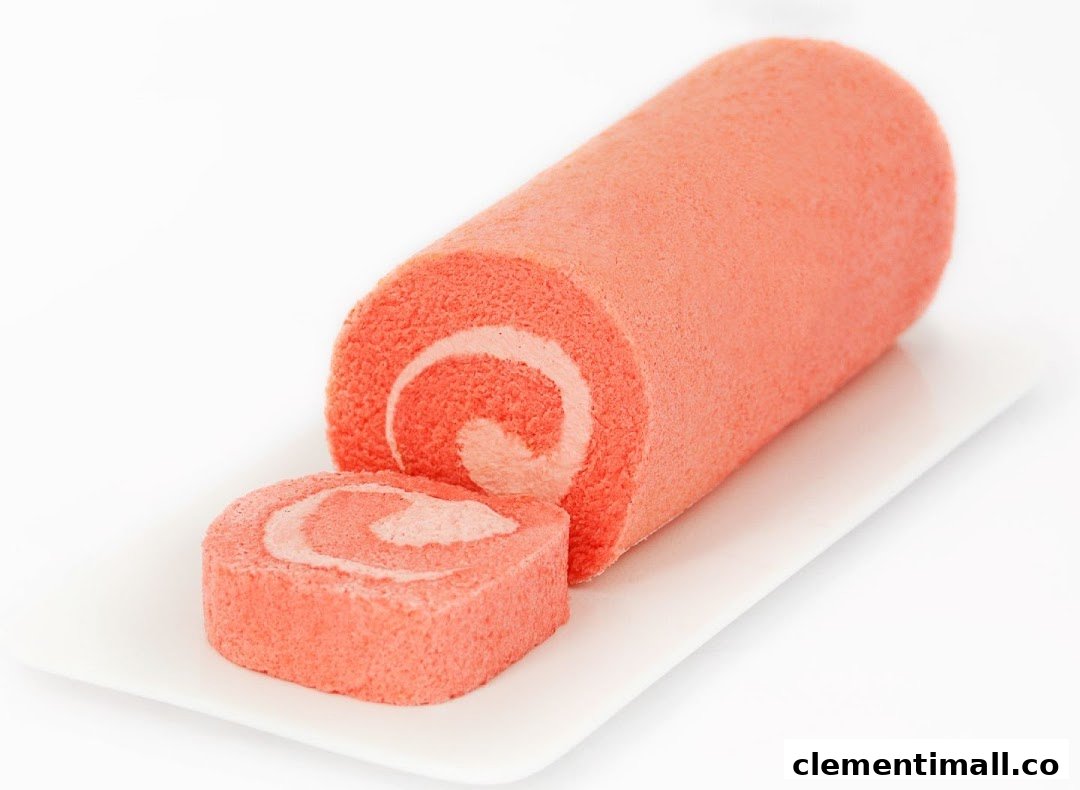 A vibrant pink cake roll with a slice cut, showcasing its creamy swirl filling on a white plate.