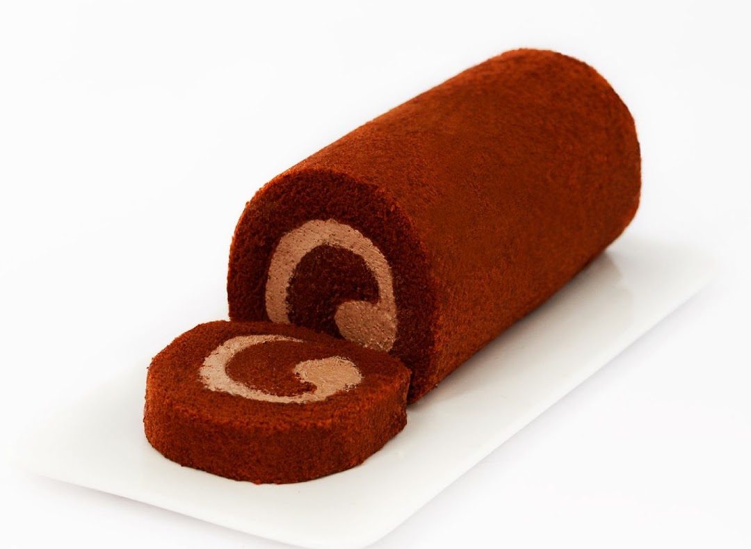 A chocolate cake roll with a slice cut off, revealing creamy filling on a white plate.