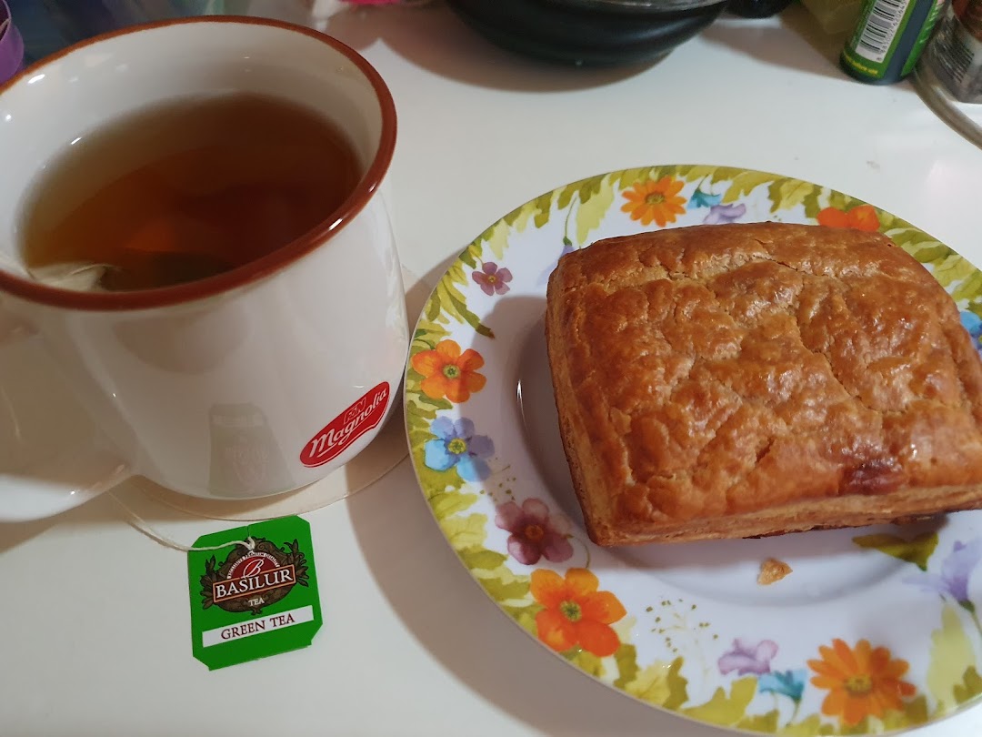 A golden-brown pastry on a floral plate next to a cup of tea with a tea bag.