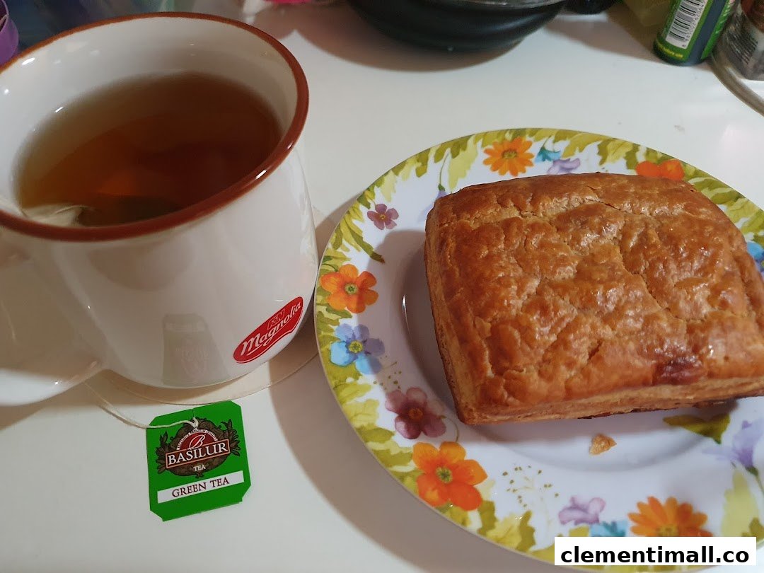 A golden-brown pastry on a floral plate next to a cup of tea with a tea bag.