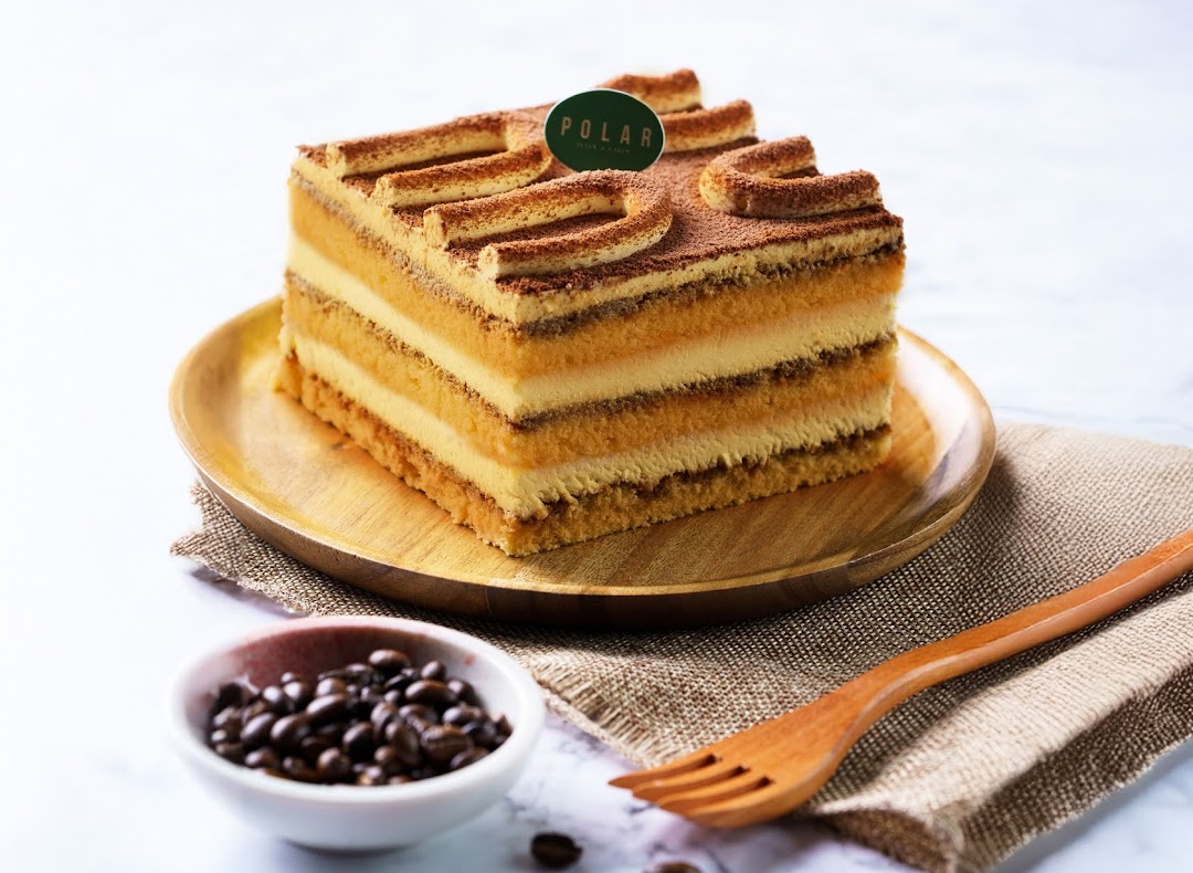 A delicious multi-layered cake with cocoa powder and a Polar brand tag, presented on a wooden plate.