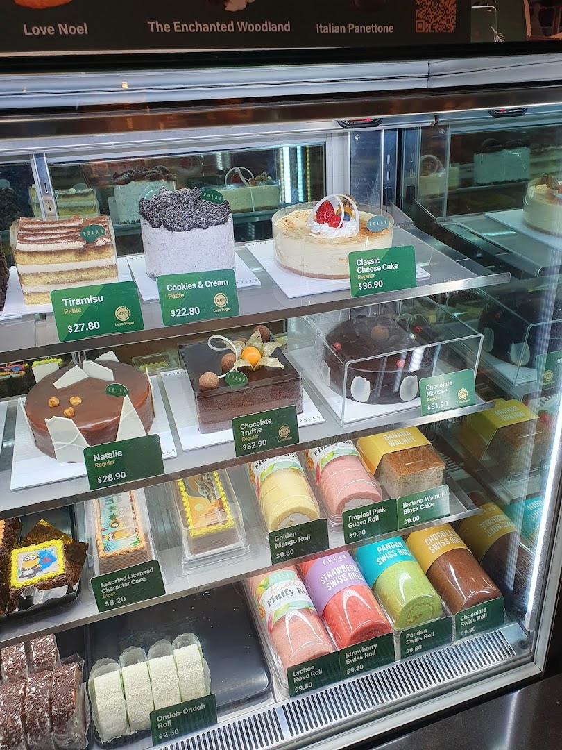A vibrant display case showcasing a variety of cakes, swiss rolls, and pastries with prices.