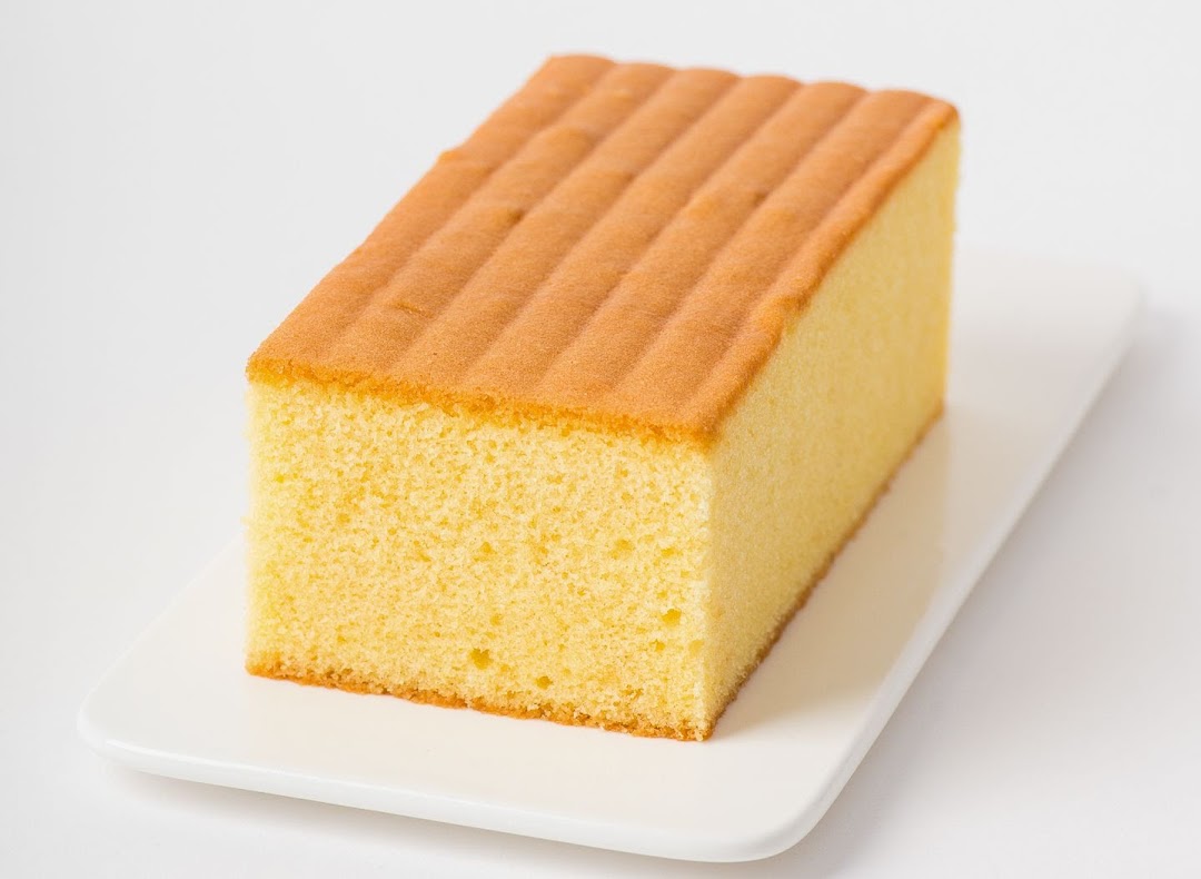 A rectangular golden sponge cake with a ribbed top, presented on a white rectangular plate.