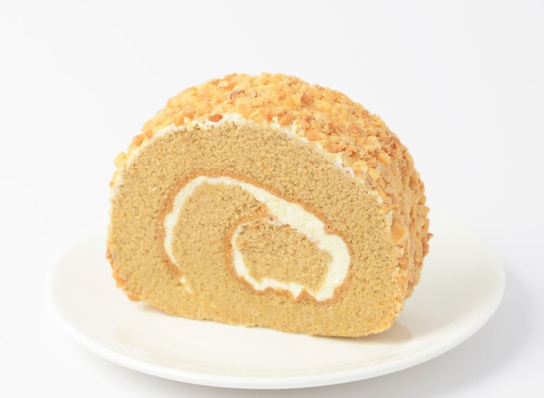 A delicious slice of nut-topped cake roll with cream filling on a white plate.