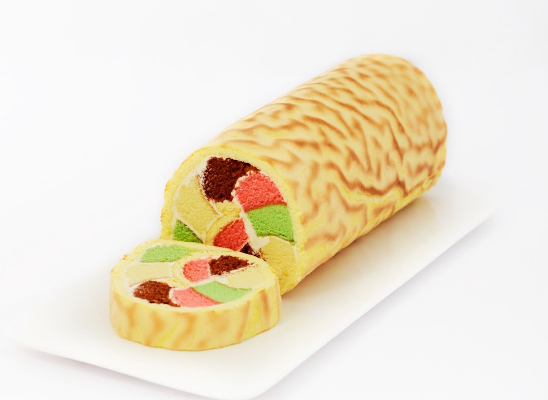 A vibrant, multi-colored cake roll with a slice cut, presented on a white rectangular plate.