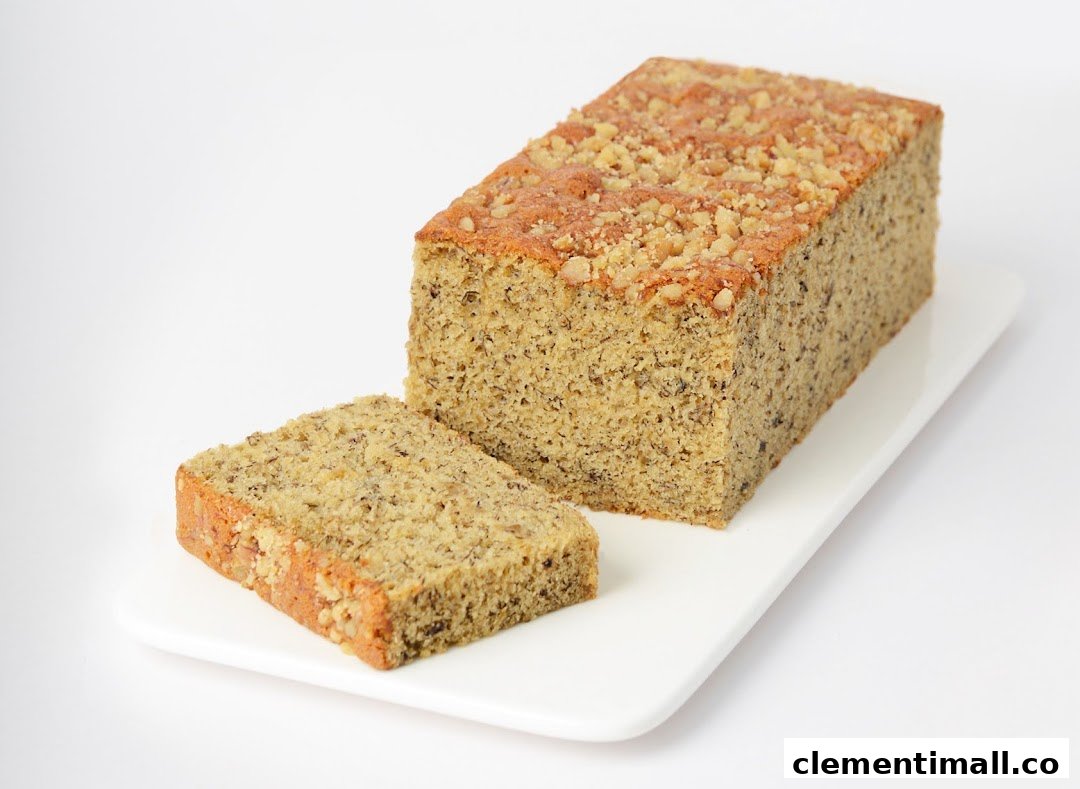 A delicious banana bread loaf with a slice cut, topped with nuts, on a white serving dish.