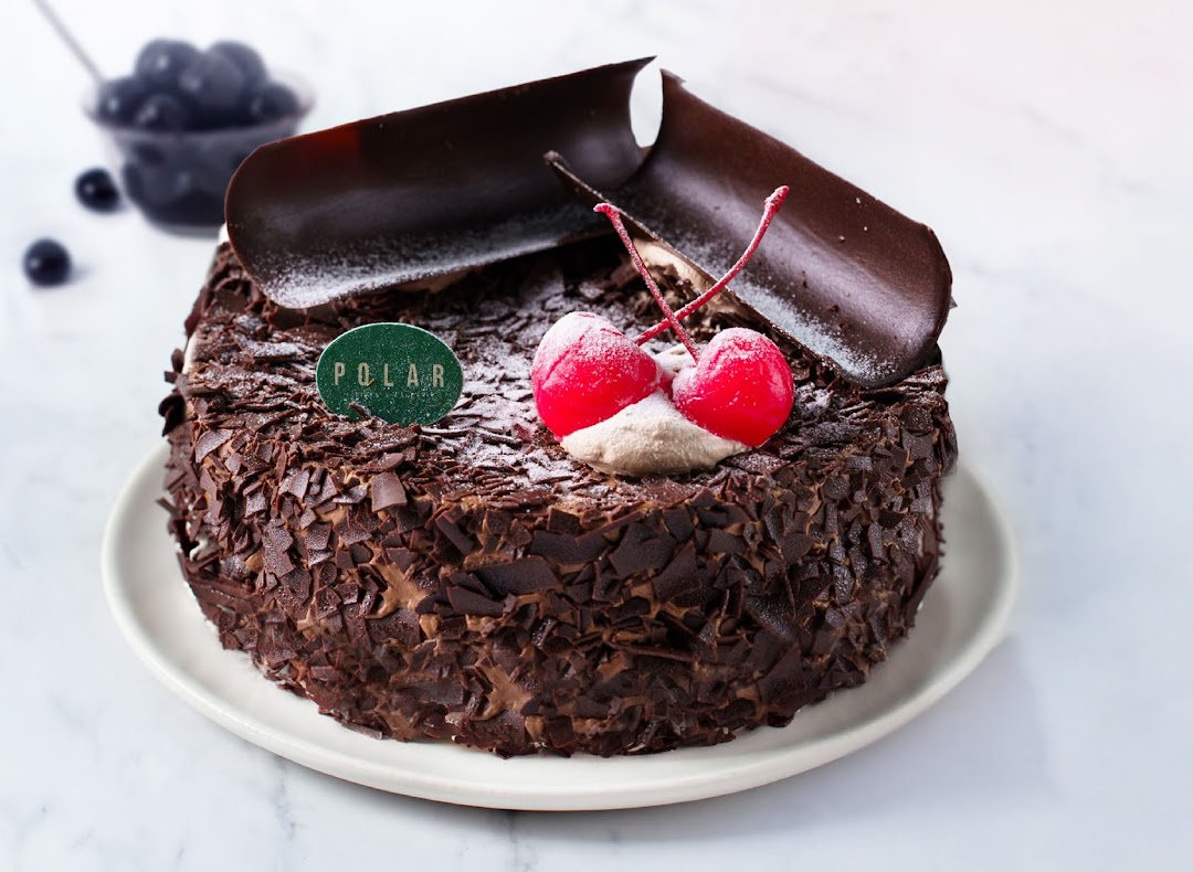 A decadent chocolate cake adorned with chocolate shavings, cherries, and a 'Polar' brand tag.