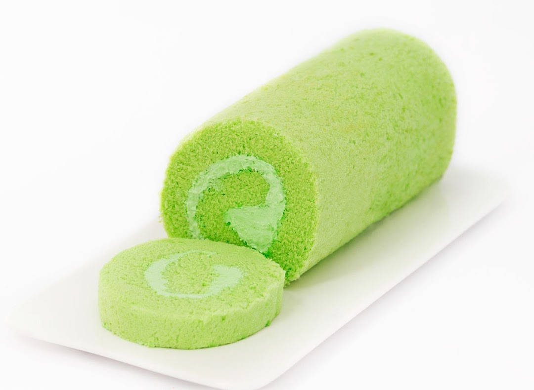A vibrant green cake roll with a slice cut, displayed on a white plate.