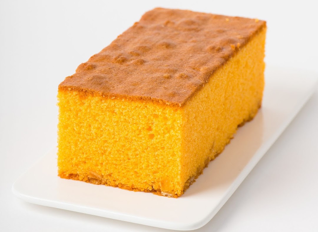 A rectangular orange cake with a golden-brown top, presented on a white plate.