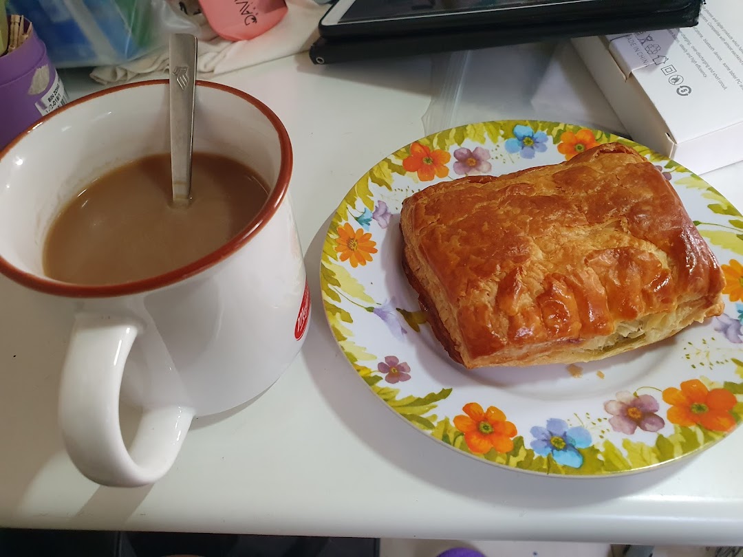 A golden-brown pastry on a floral plate next to a mug of coffee or tea.