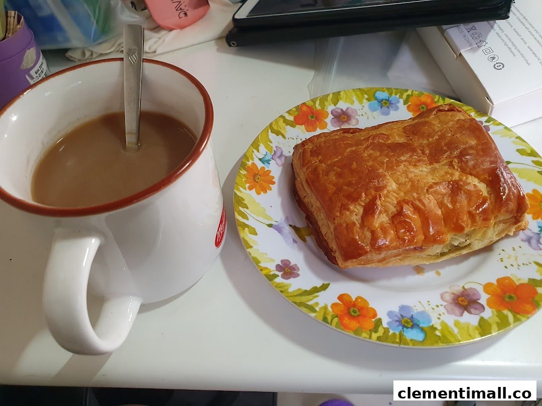A golden-brown pastry on a floral plate next to a mug of coffee or tea.