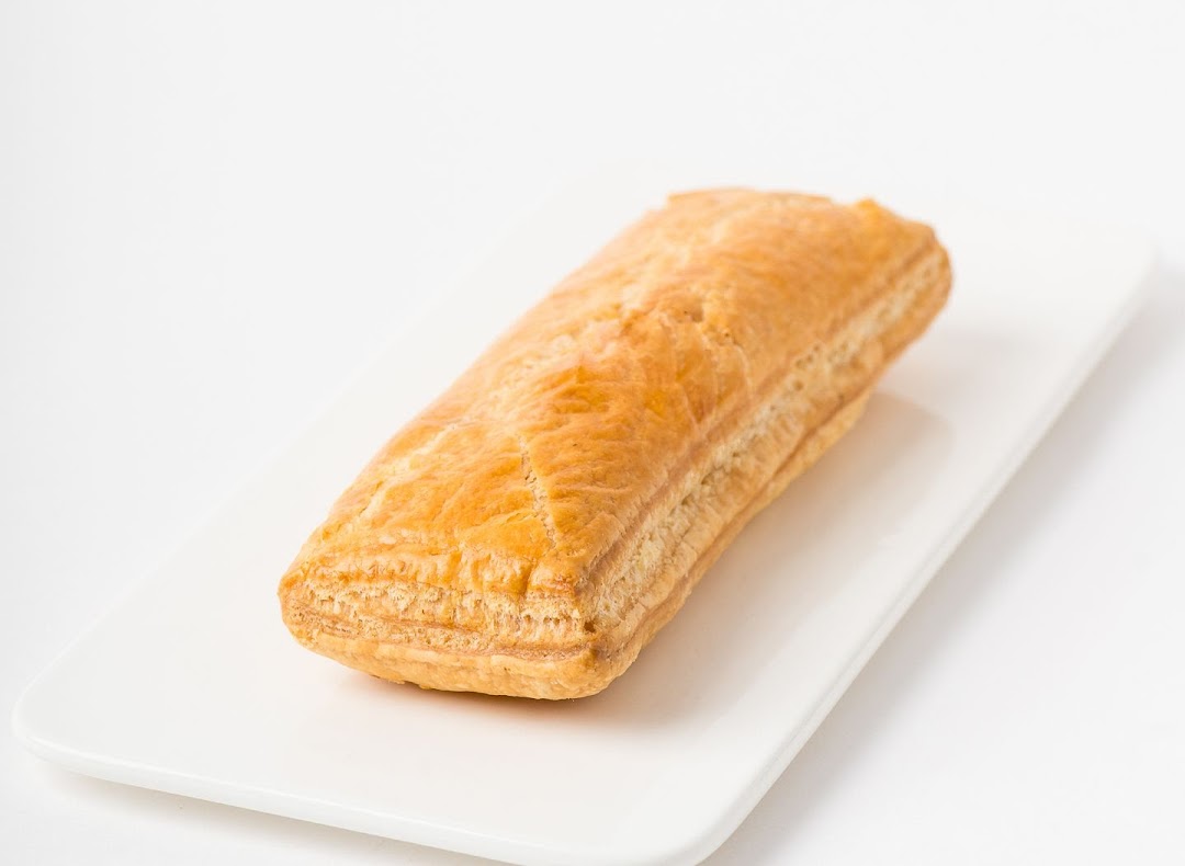 A golden-brown, flaky pastry, likely a puff or sausage roll, presented on a white rectangular plate.