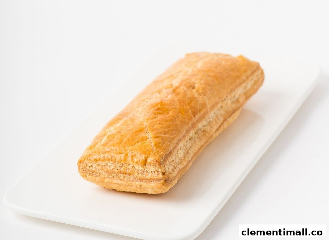 A golden-brown, flaky pastry, likely a puff or sausage roll, presented on a white rectangular plate.
