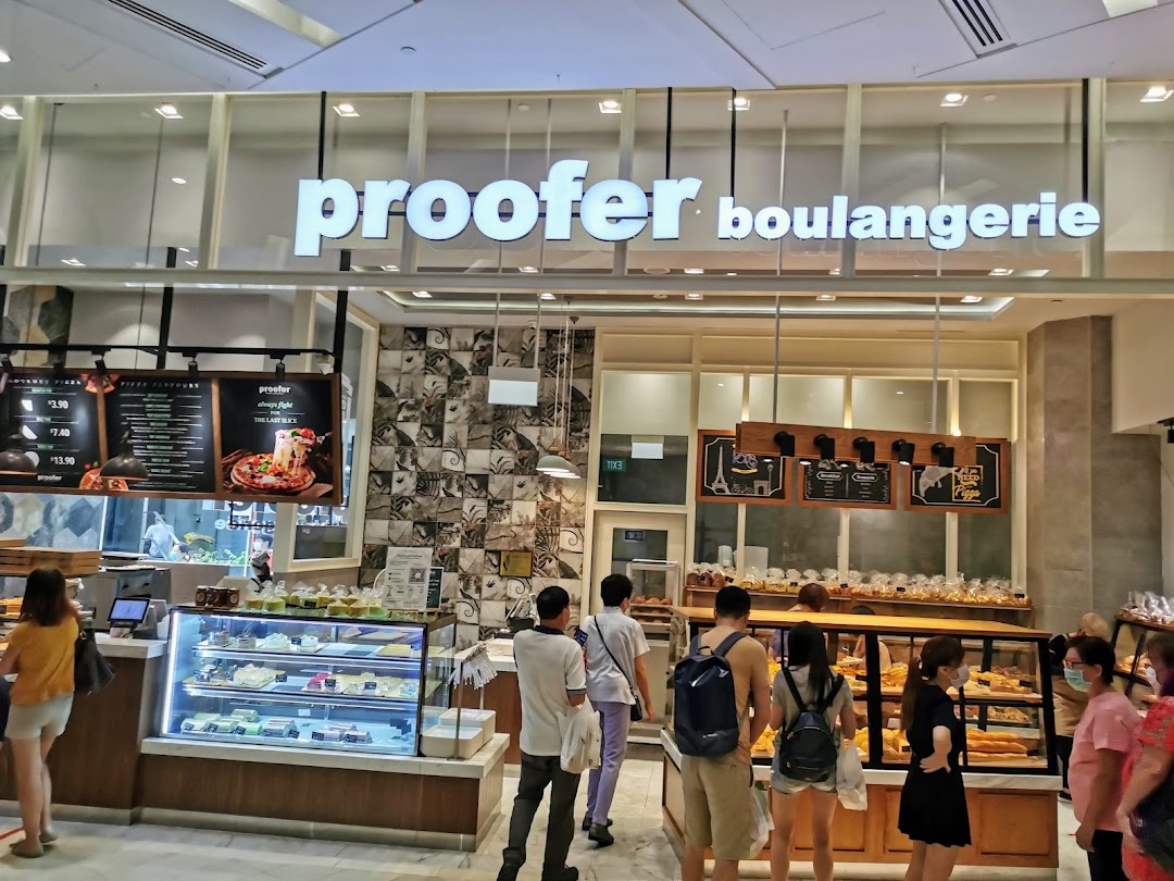 The vibrant storefront of Proofer Boulangerie, showcasing its bakery and pizza offerings with customers browsing.