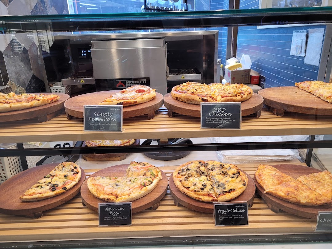 A display case filled with various freshly baked pizzas and savory items at Proofer Boulangerie.