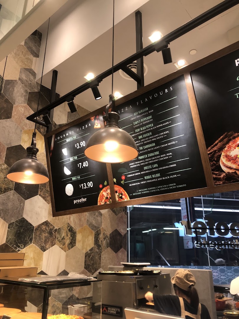 A menu board displaying pizza sizes and flavors, with a staff member preparing food.