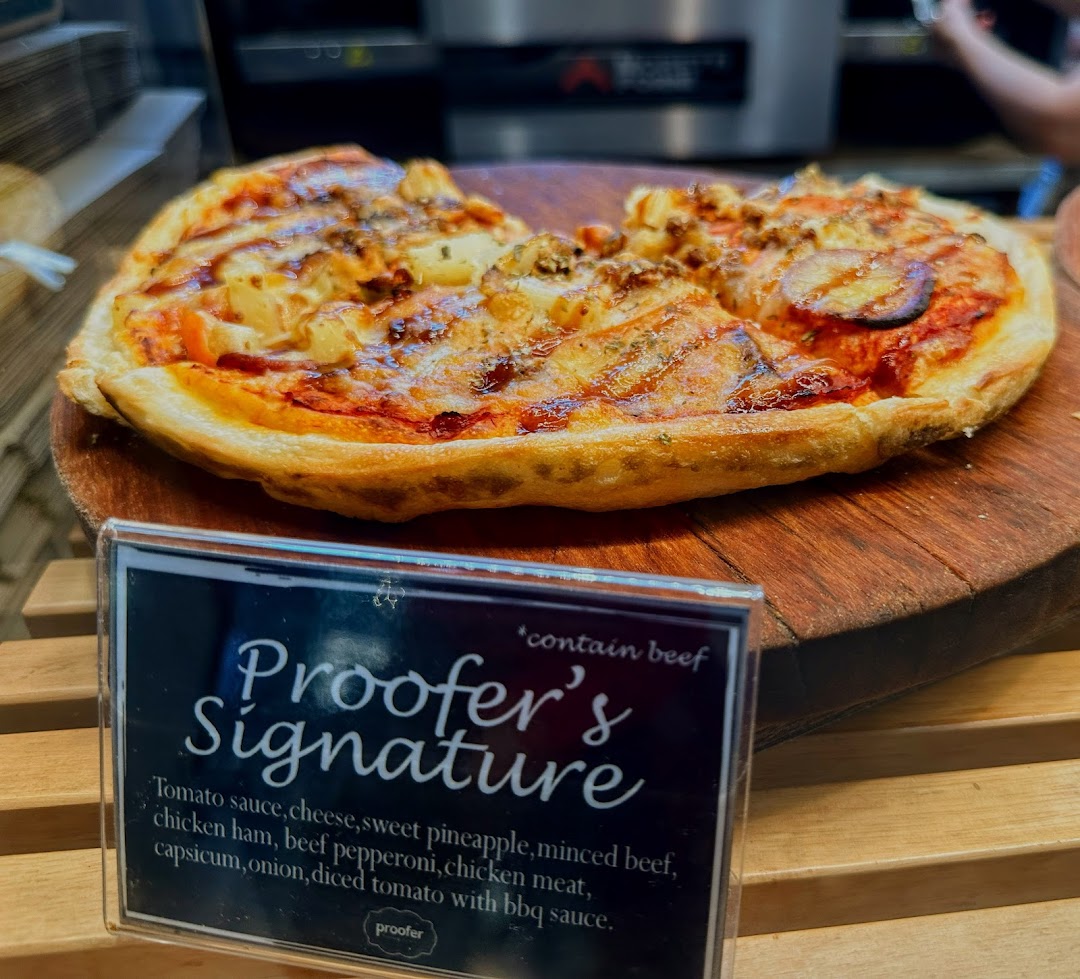 A Proofer's Signature pizza with various toppings displayed on a wooden board with its description.