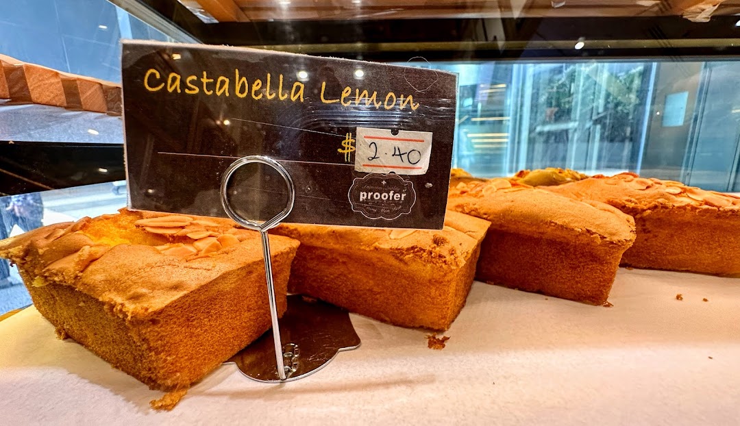 Close-up of freshly baked Castabella Lemon loaves displayed in a bakery showcase with a price tag.