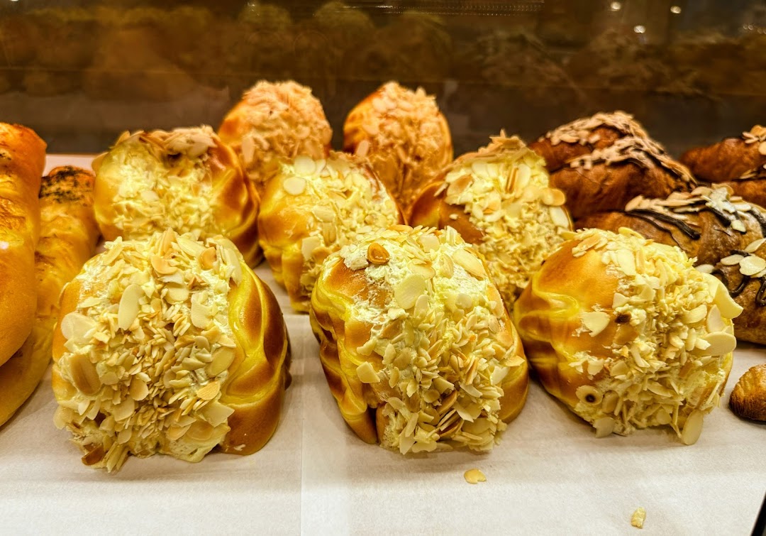Close-up of golden-brown pastries topped with generous almond flakes in a bakery display.