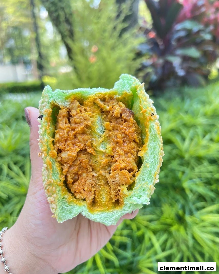A hand holds a vibrant green bun filled with savory orange curry, set against a lush green background.