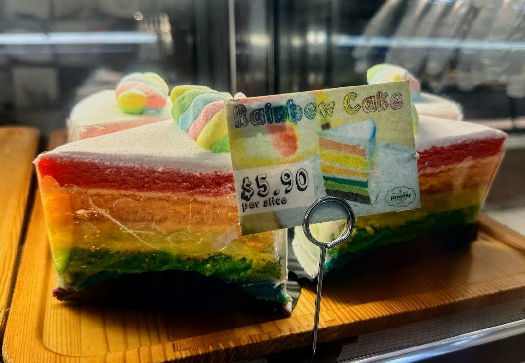 A vibrant slice of rainbow cake with a price tag displayed in a bakery.