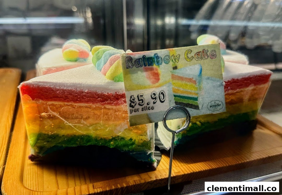 A vibrant slice of rainbow cake with a price tag displayed in a bakery.