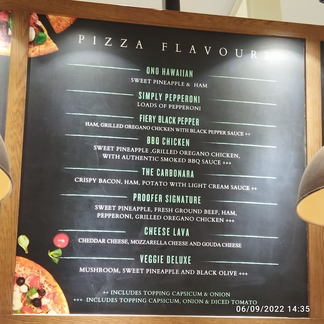 A menu board displaying various pizza flavors and their ingredients at Proofer Boulangerie.