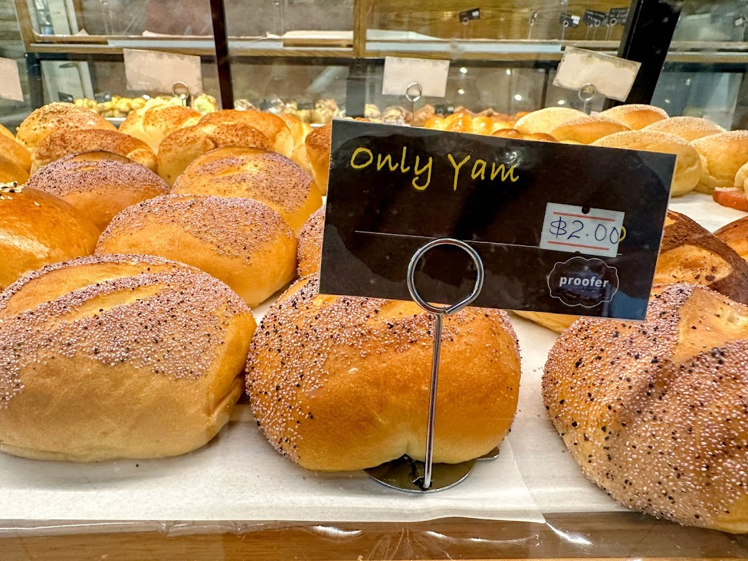 Close-up of freshly baked buns, some with toppings, displayed in a bakery case with a price tag.