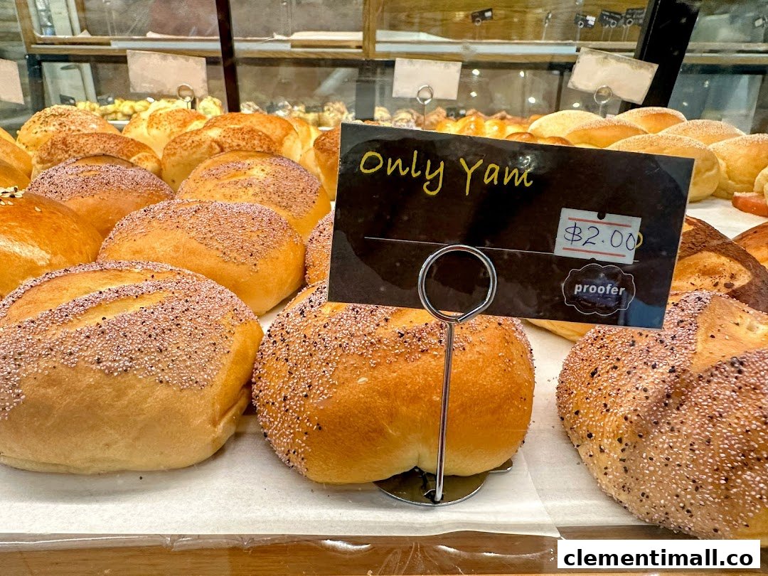 Close-up of freshly baked buns, some with toppings, displayed in a bakery case with a price tag.