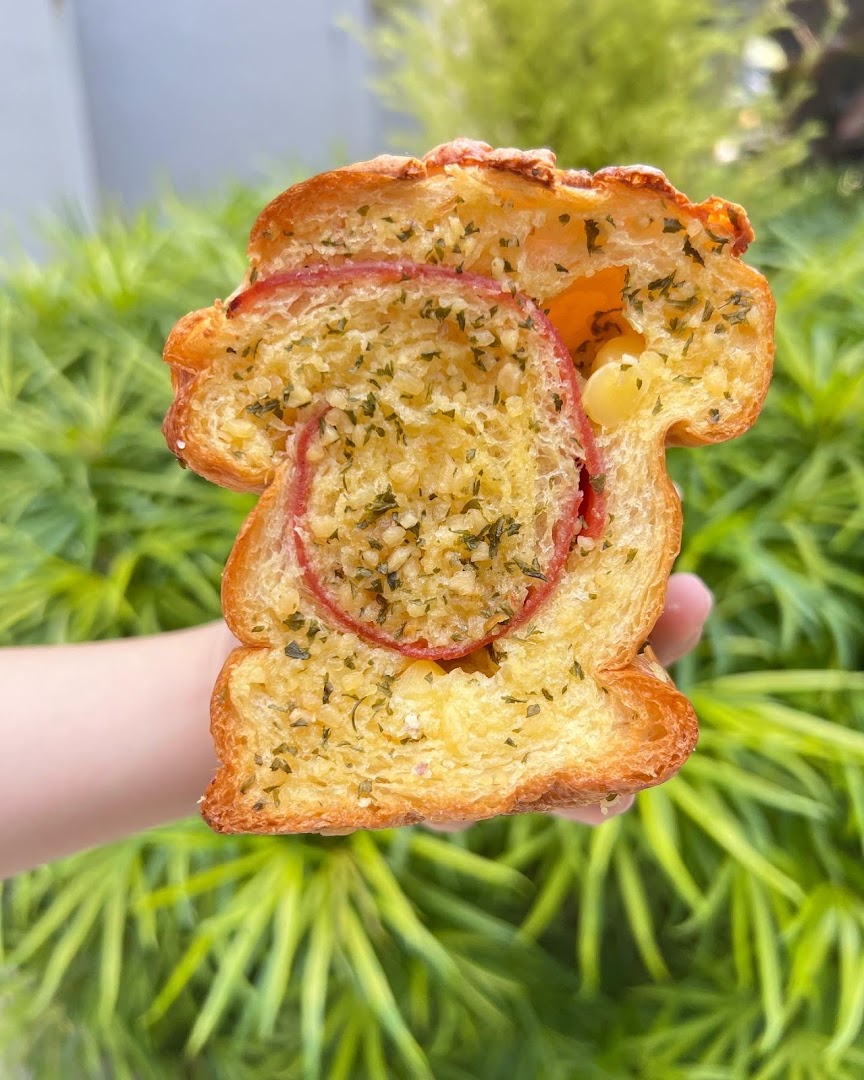 A hand holds a delicious slice of golden-brown garlic bread with a savory red filling.