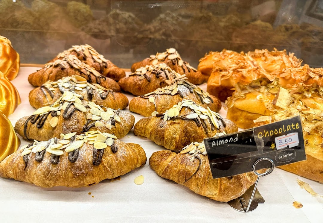 A display of freshly baked chocolate almond croissants and other golden pastries at Proofer Boulangerie.