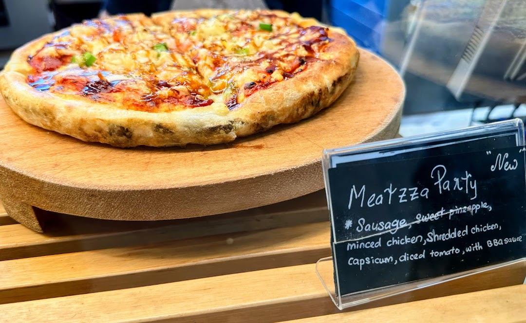 A close-up of a 'Meatzza Party' pizza on a wooden stand with its descriptive label.