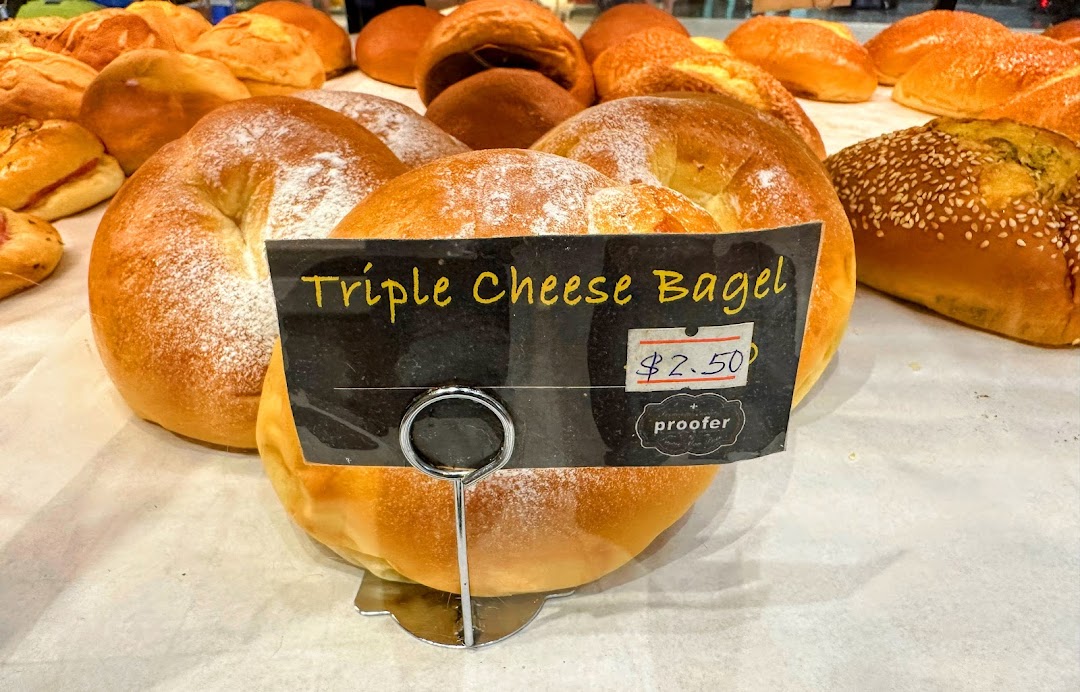 A display of freshly baked goods, featuring a Triple Cheese Bagel with a price tag.