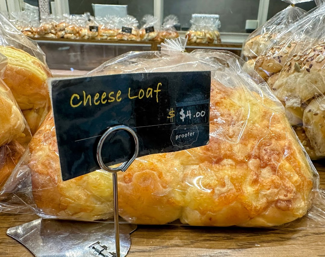 A close-up of a freshly baked Cheese Loaf from Proofer Boulangerie, priced at $4.00, displayed in a clear bag.