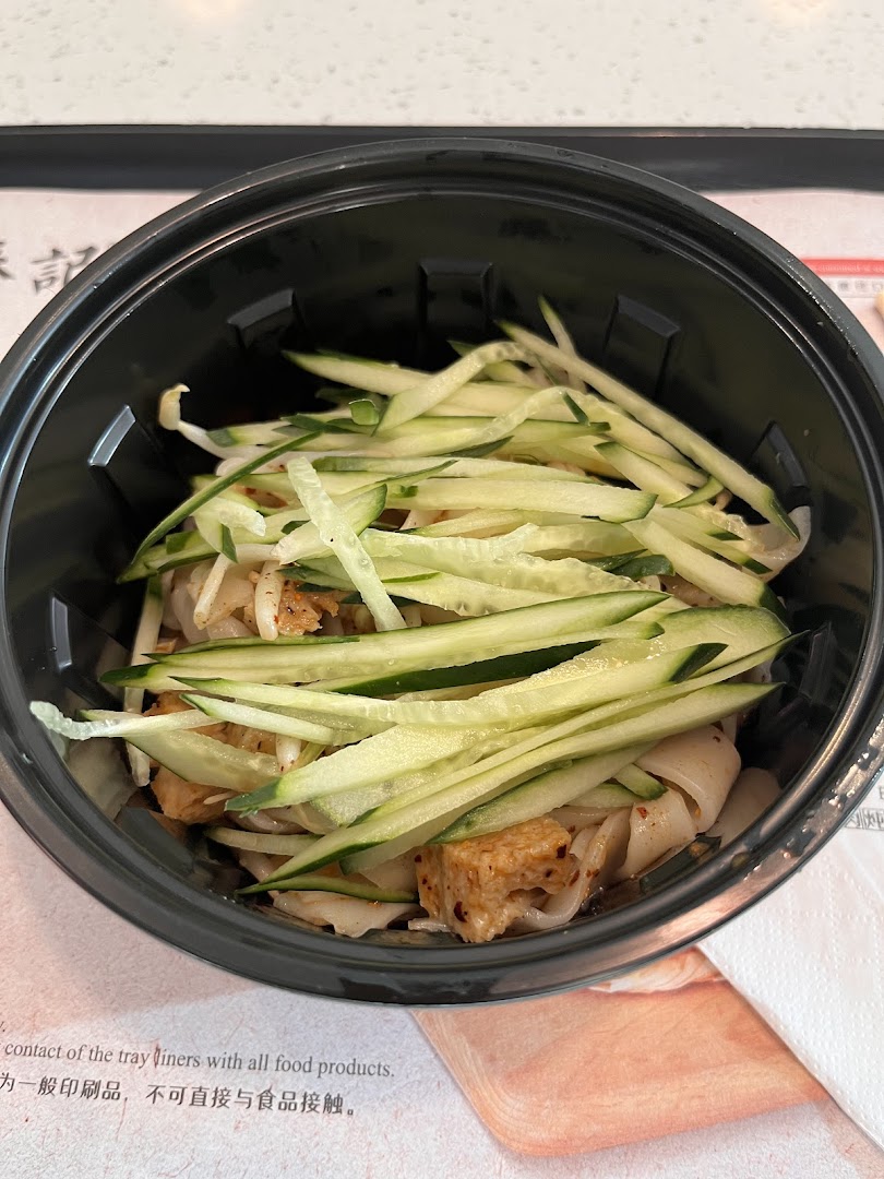 A close-up of a delicious noodle dish topped with fresh cucumber strips and tofu in a black bowl.