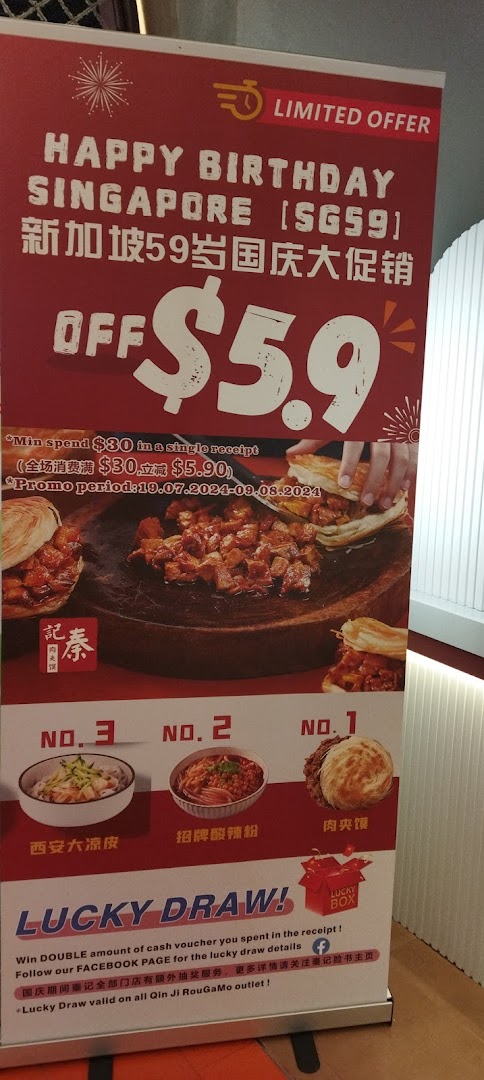 A promotional standee for Qin Ji Rougamo featuring a Singapore National Day offer and a lucky draw.