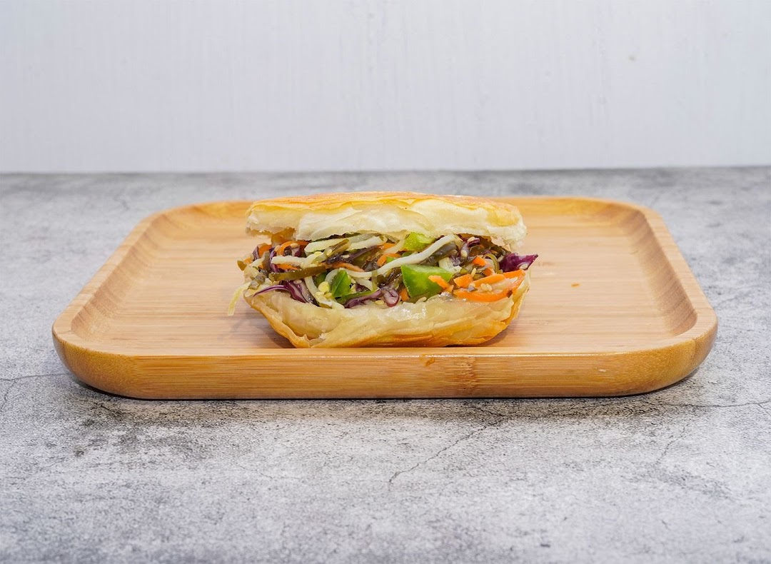 A close-up of a savory roujiamo-style bun filled with fresh vegetables on a wooden plate.