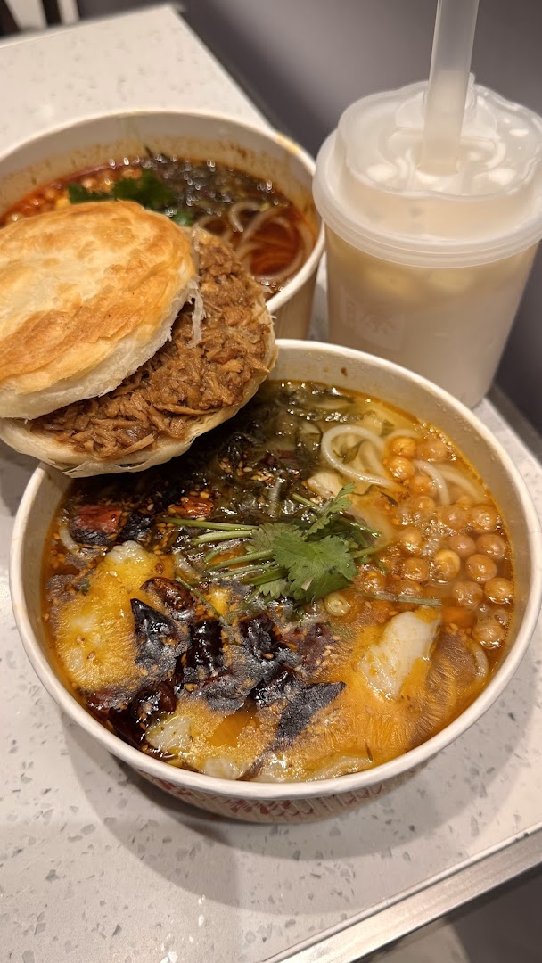 A delicious spread featuring a roujiamo, spicy noodles, and a refreshing drink on a counter.