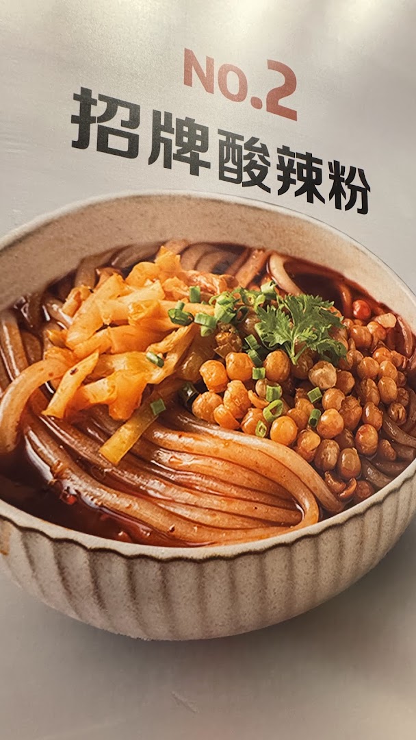 A vibrant bowl of sour and spicy noodles, topped with pickled vegetables and crispy chickpeas.